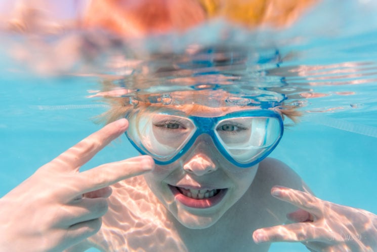 Underwater view of redhaired boy diving in cool blue holiday swimming pool