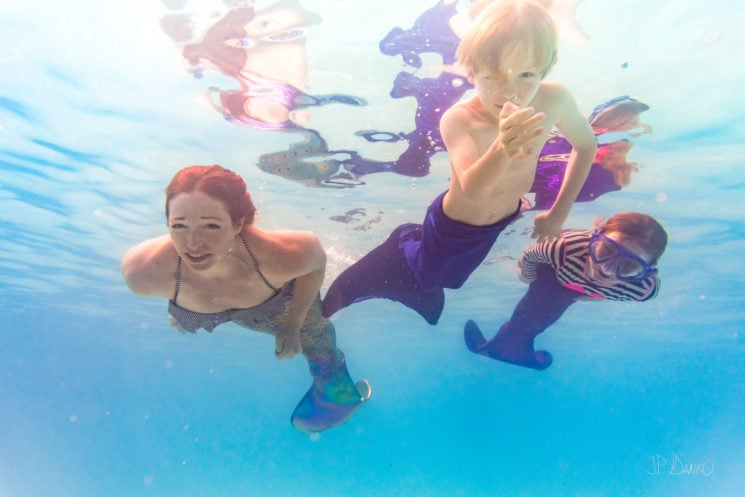 Underwater view of mom son and daughter on holiday swimming in pool with colorful mermaid tails
