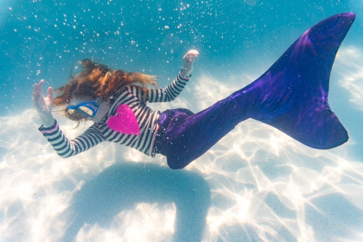 Underwater view of girl on holiday swimming in pool with colorful mermaid tail