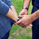 policemans hands putting cuffs on a suspect