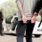 policewoman walking with criminal in handcuffs while partner waiting them near car