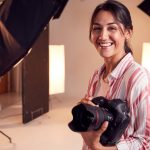 Portrait Of Smiling Female Photographer Standing In Studio With Camera