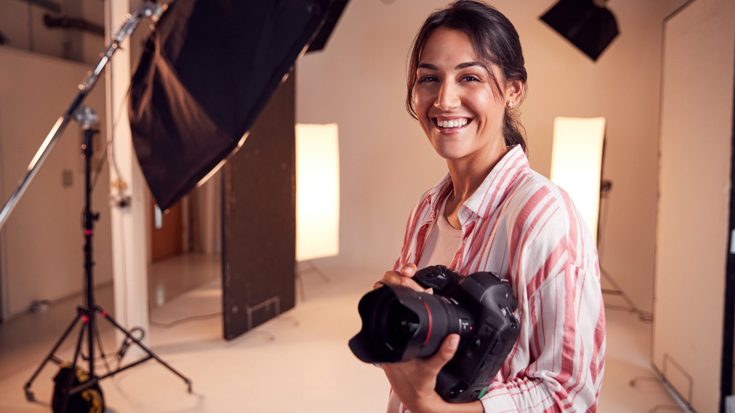 Portrait Of Smiling Female Photographer Standing In Studio With Camera
