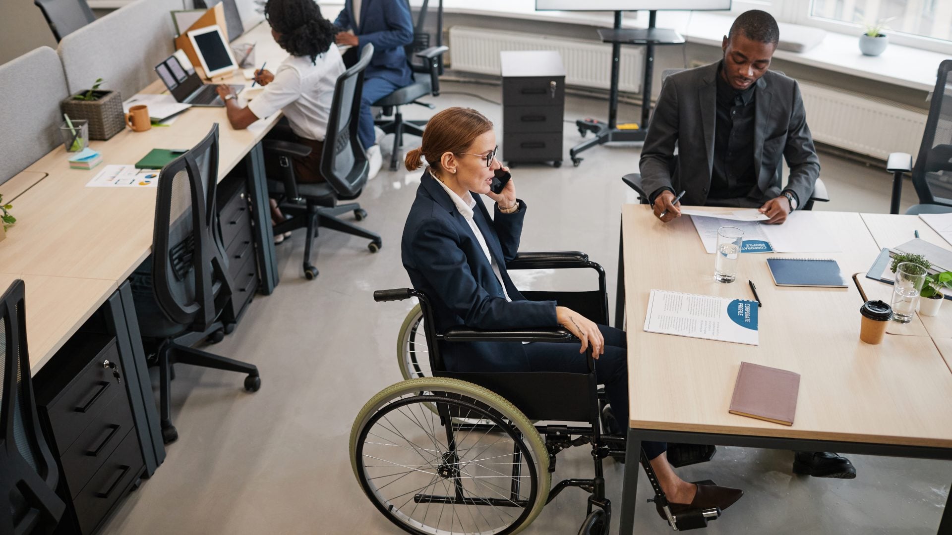 High angle portrait of successful businesswoman using wheelchair while managing at business meeting in office and talking to team, copy space