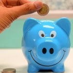 Hand inserting a coin into a blue piggy bank for savings and money management.