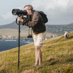 Photographer with a camera on tripod capturing scenic coastal views, highlighting the essence of landscape photography.