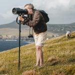 Photographer with a camera on tripod capturing scenic coastal views, highlighting the essence of landscape photography.