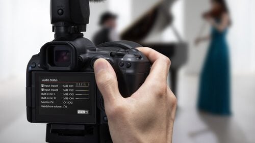 A person recording a live music performance with a Canon EOS R5 Mark II camera, displaying audio settings on the screen.