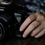 A close-up of a person's hand resting on a Canon EOS 1000S film camera.