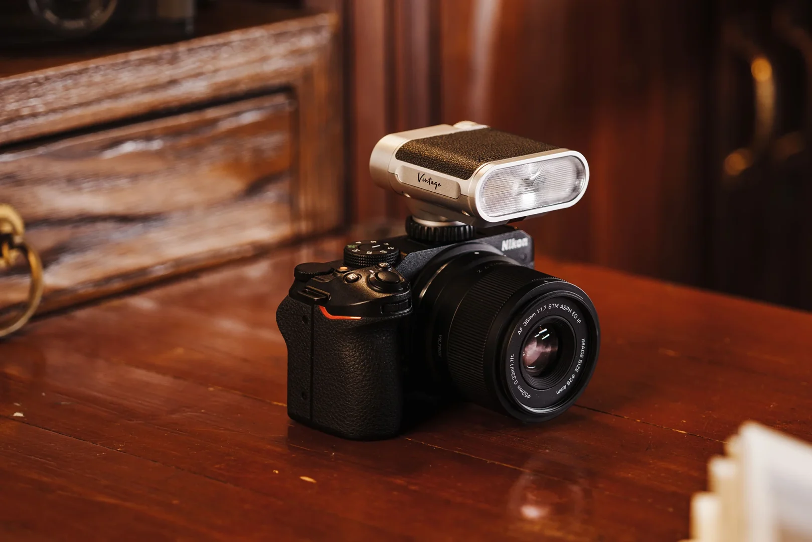 A Nikon mirrorless camera with a Viltrox Z1 Vintage flash mounted on top, placed on a wooden surface with a retro-style background.