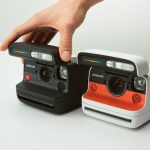A close-up image of two Polaroid Flip instant cameras, one in black and the other in white with a red accent, placed on a white surface.