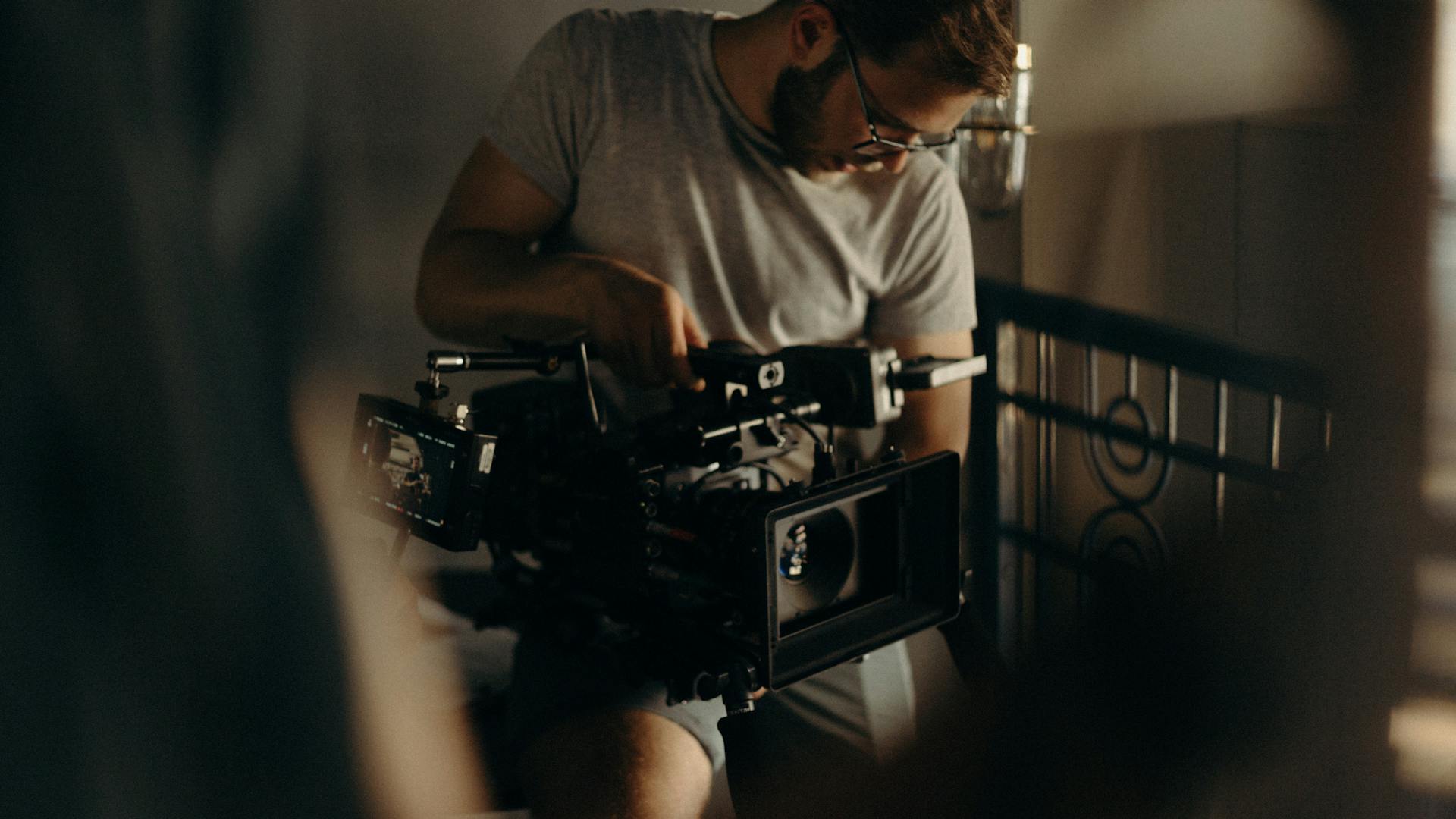 Man adjusting a professional video camera in an indoor setting, filmmaking.
