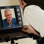 A person leans over a laptop running Capture One software, editing a portrait using AI-powered retouching tools, with image thumbnails and adjustment panels visible on the screen.