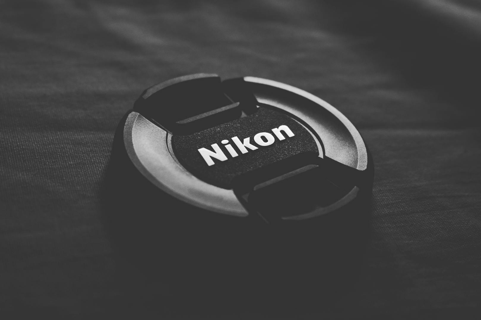 Black Nikon lens cap on dark textured surface. Minimalist and sleek design.