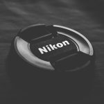 Black Nikon lens cap on dark textured surface. Minimalist and sleek design.