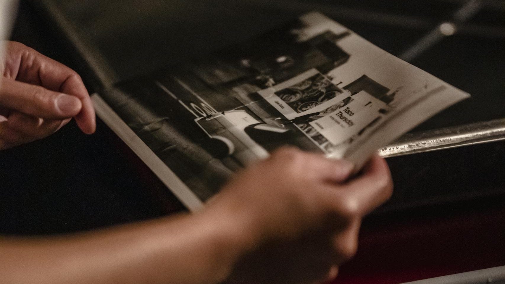 Hands of an adult developing a black and white photo in a darkroom setting.