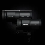 Two black Profoto B20 and B30 OCF lights side by side against a dark background, showcasing their compact, cylindrical design and LED indicator panel.