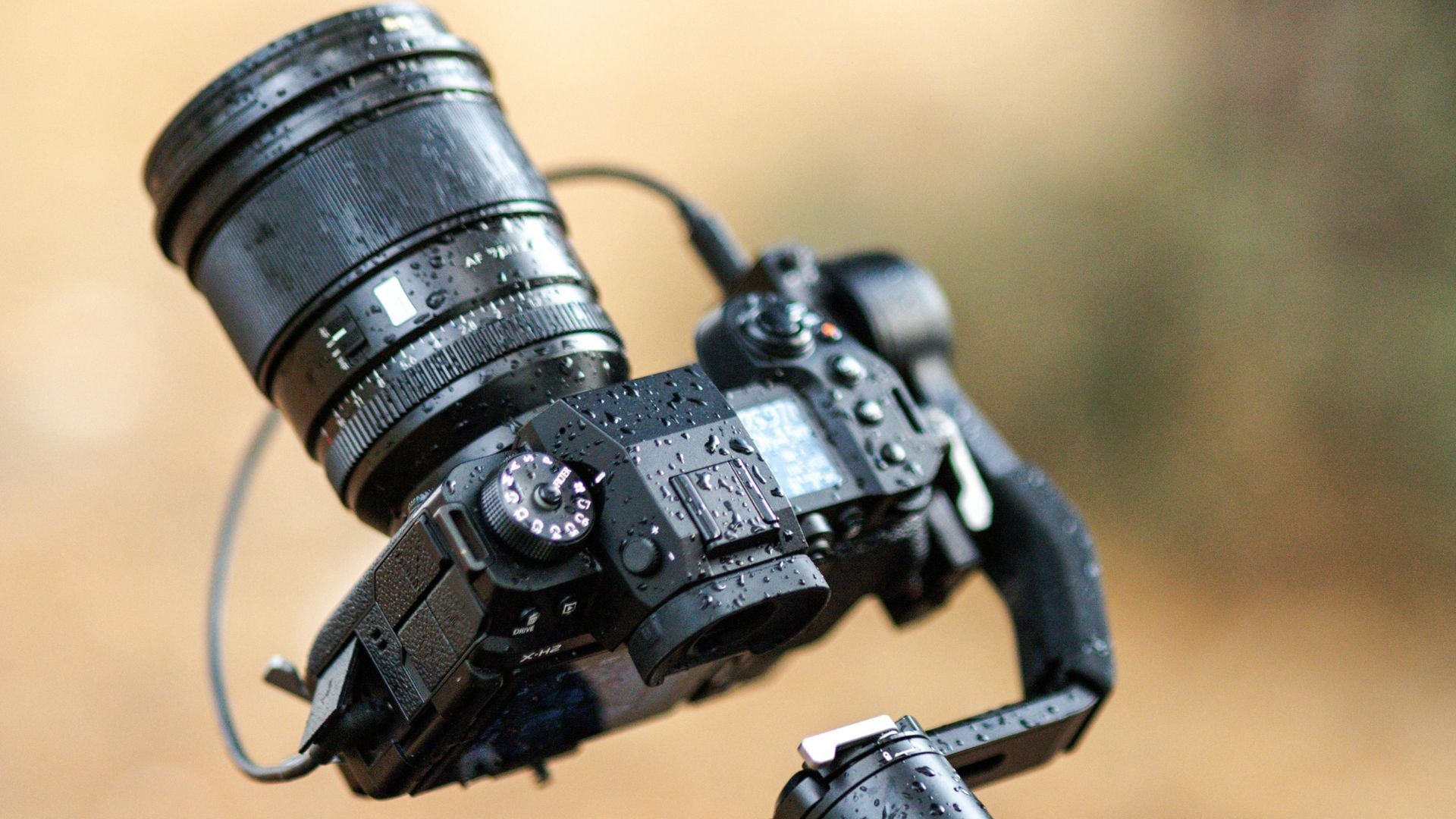 A close-up of a camera with droplets of water on its body and lens, demonstrating its ability to withstand rain and protect internal components.