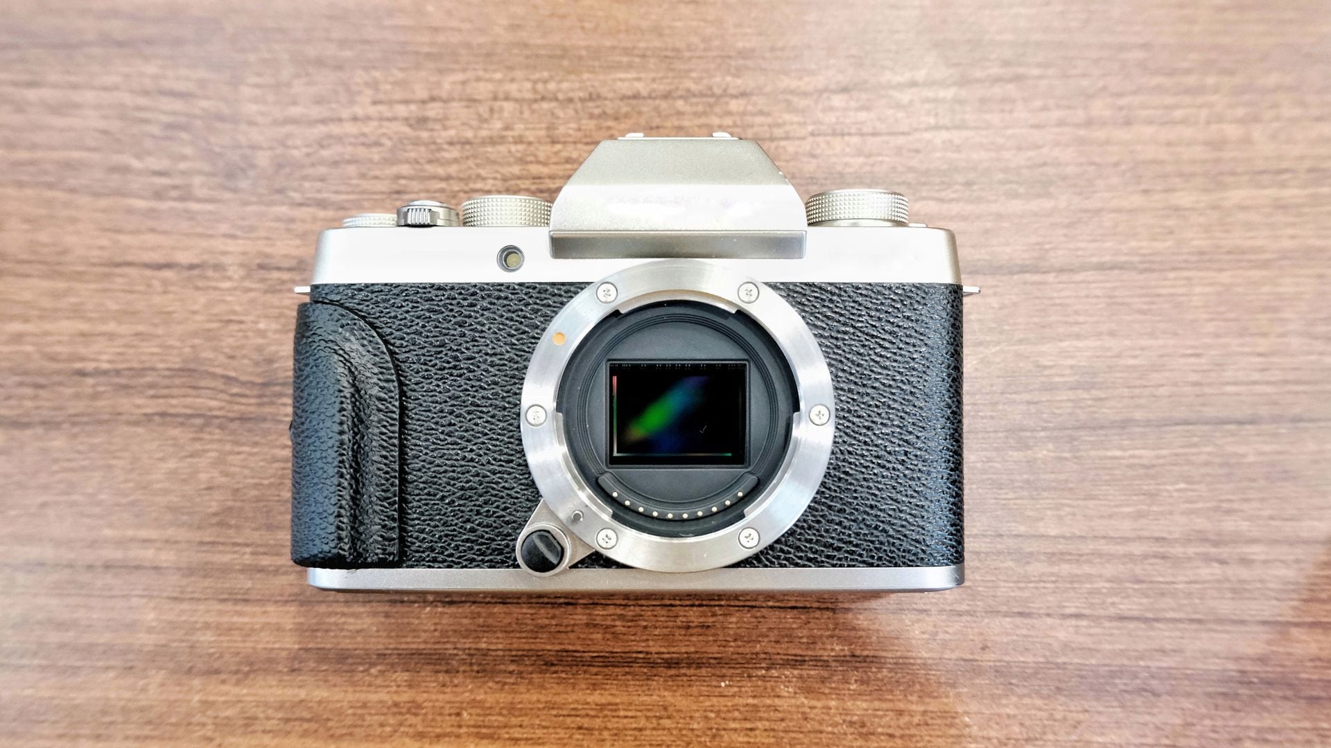 A top-down shot of the Fujifilm X-T1 mirrorless camera with the lens removed, highlighting its APS-C sensor. The classic silver-and-black body and textured grip reflect the retro-inspired design Fuji is known for.