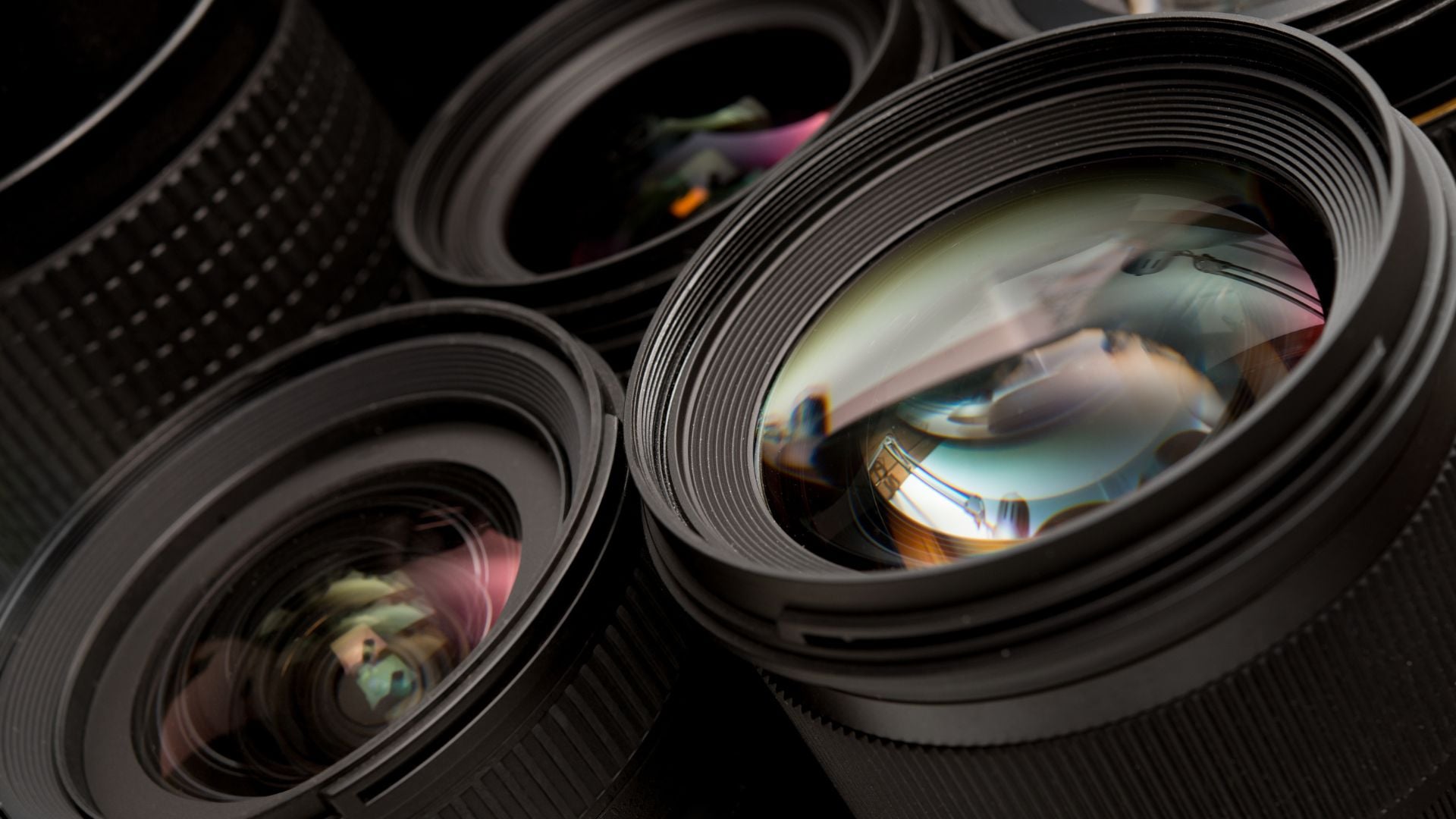 A detailed view of several camera lenses stacked together, showcasing their intricate lens elements and the various coatings reflecting light, highlighting their role in capturing stunning photographs with incredible detail and clarity.