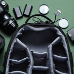 A photography bag opened with organized compartments, surrounded by camera equipment including lenses, battery packs, and filters.