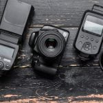 A flat lay shot of a camera with accessories like a flash, lens filters, and a tripod, arranged on a wooden surface.