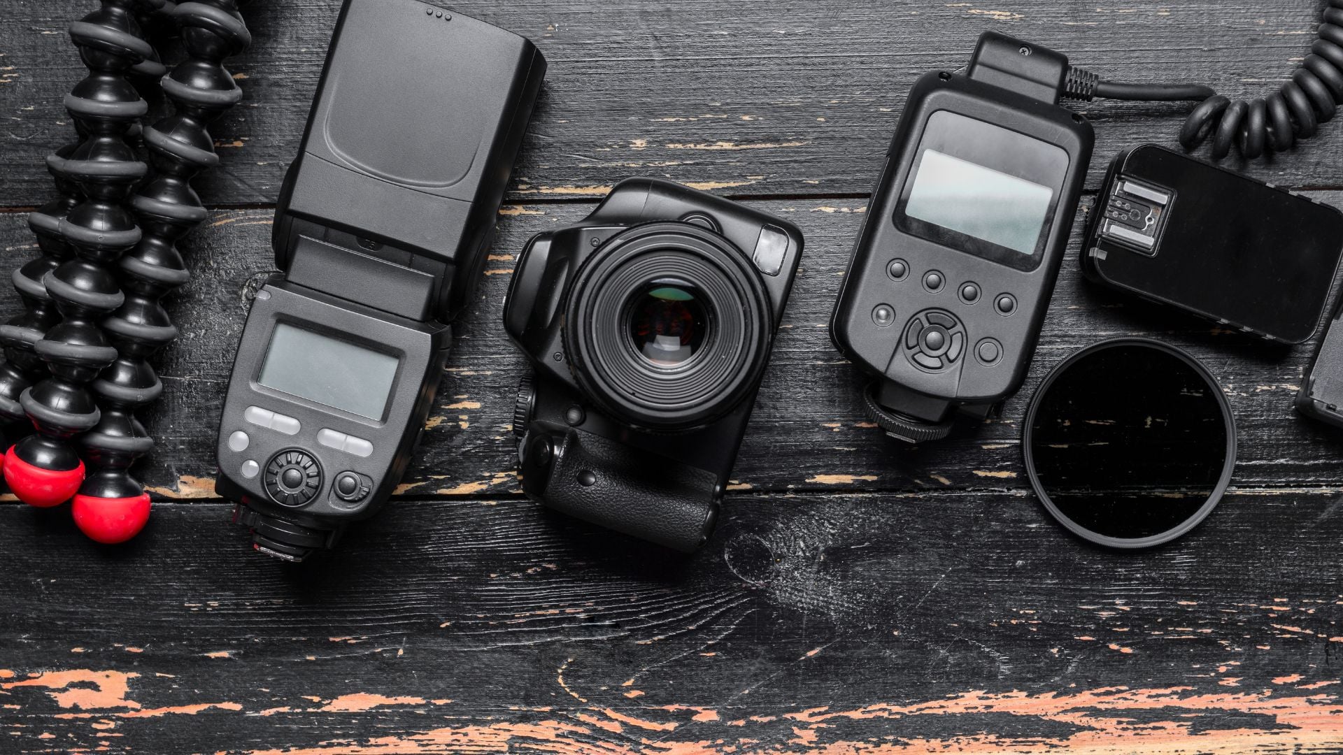 A flat lay shot of a camera with accessories like a flash, lens filters, and a tripod, arranged on a wooden surface.