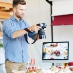 A photographer capturing a beautiful food scene with various dishes, while adjusting the camera settings in a bright studio environment.