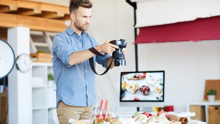 A photographer capturing a beautiful food scene with various dishes, while adjusting the camera settings in a bright studio environment.