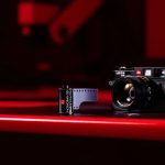 A Leica M-series camera with a black and white Leica Monopan 50 film roll placed beside it, all bathed in soft red lighting, showcasing the classic and modern fusion in photography gear.