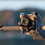 Compact DJI Mini 5 Pro quadcopter drone featuring prominent camera gimbal and stabilization system captured during warm golden hour lighting conditions.