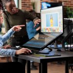 Two women collaborating on photo editing at a desk, working on a photo of a model on a large screen, demonstrating teamwork in the creative process with free photo editing software.