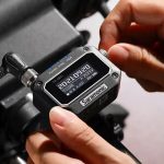 Hands holding compact Saramonic digital audio recorder with LCD display showing timecode, connected cables, and professional recording interface for content creation.