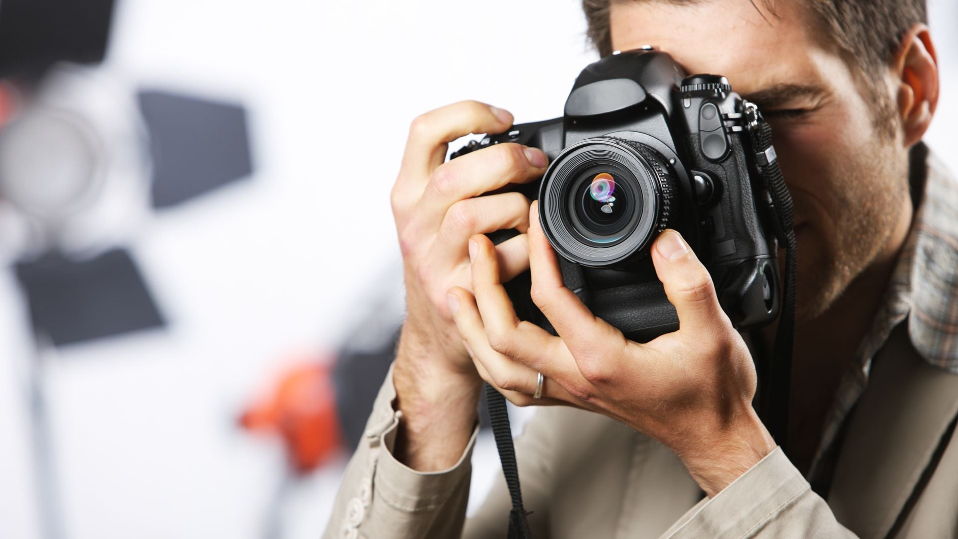 A person holding a Canon DSLR camera while taking a photo outdoors. The subject is focused, with a blurred background of nature and flowers. This image emphasizes a professional camera used for high-quality photography.
