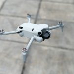 Clean white quadcopter drone with camera gimbal hovering above gray stone tile patio surface showing sleek modern design and stabilization system.