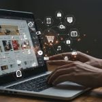 Hands using laptop displaying online shopping website with floating digital icons including shopping cart, security lock, payment, storefront, and settings representing e-commerce features with glowing network connections.