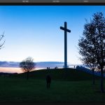 Dark photo editing interface showing landscape image of large cross silhouette at sunset with people on green hill, layers panel and adjustment filters visible.