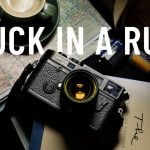Vintage Leica M6 rangefinder camera with yellow lens on map beside green coffee cup, film rolls, handwritten notes creating creative photography travel inspiration flatlay.