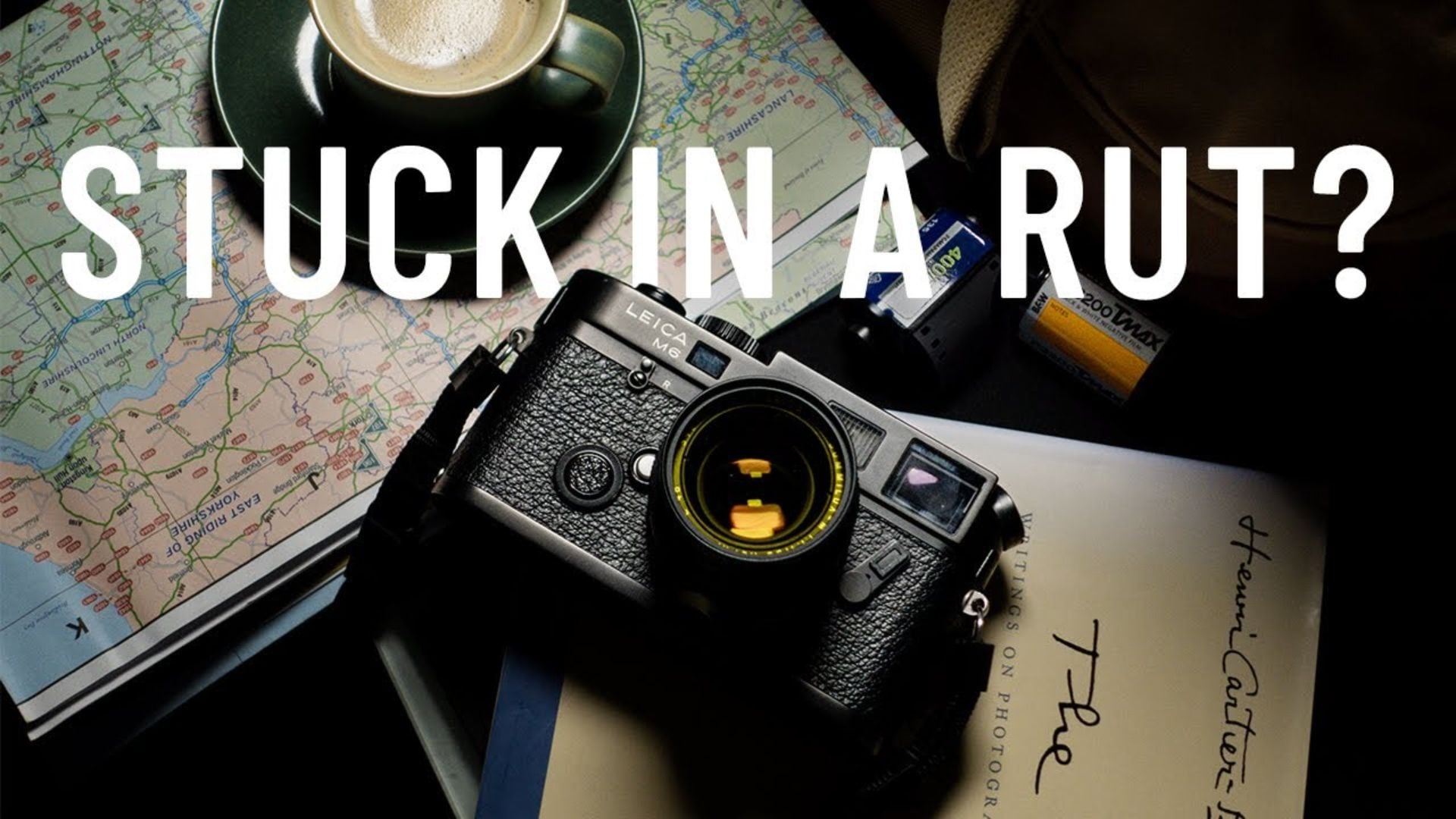 Vintage Leica M6 rangefinder camera with yellow lens on map beside green coffee cup, film rolls, handwritten notes creating creative photography travel inspiration flatlay.