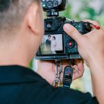Person views back of DSLR camera LCD screen showing wedding couple portrait while outdoors with green blurred natural background.