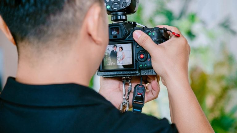 Person views back of DSLR camera LCD screen showing wedding couple portrait while outdoors with green blurred natural background.