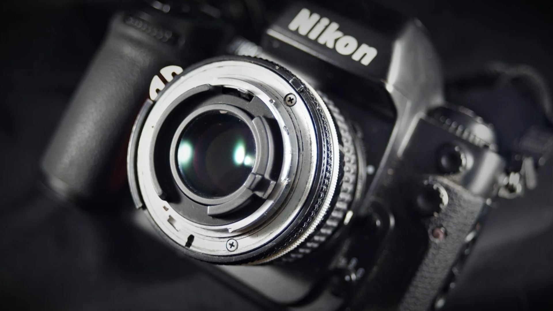 Macro view of Nikon DSLR camera body showing silver lens mount, electronic contacts, and brand name without attached lens in focus.