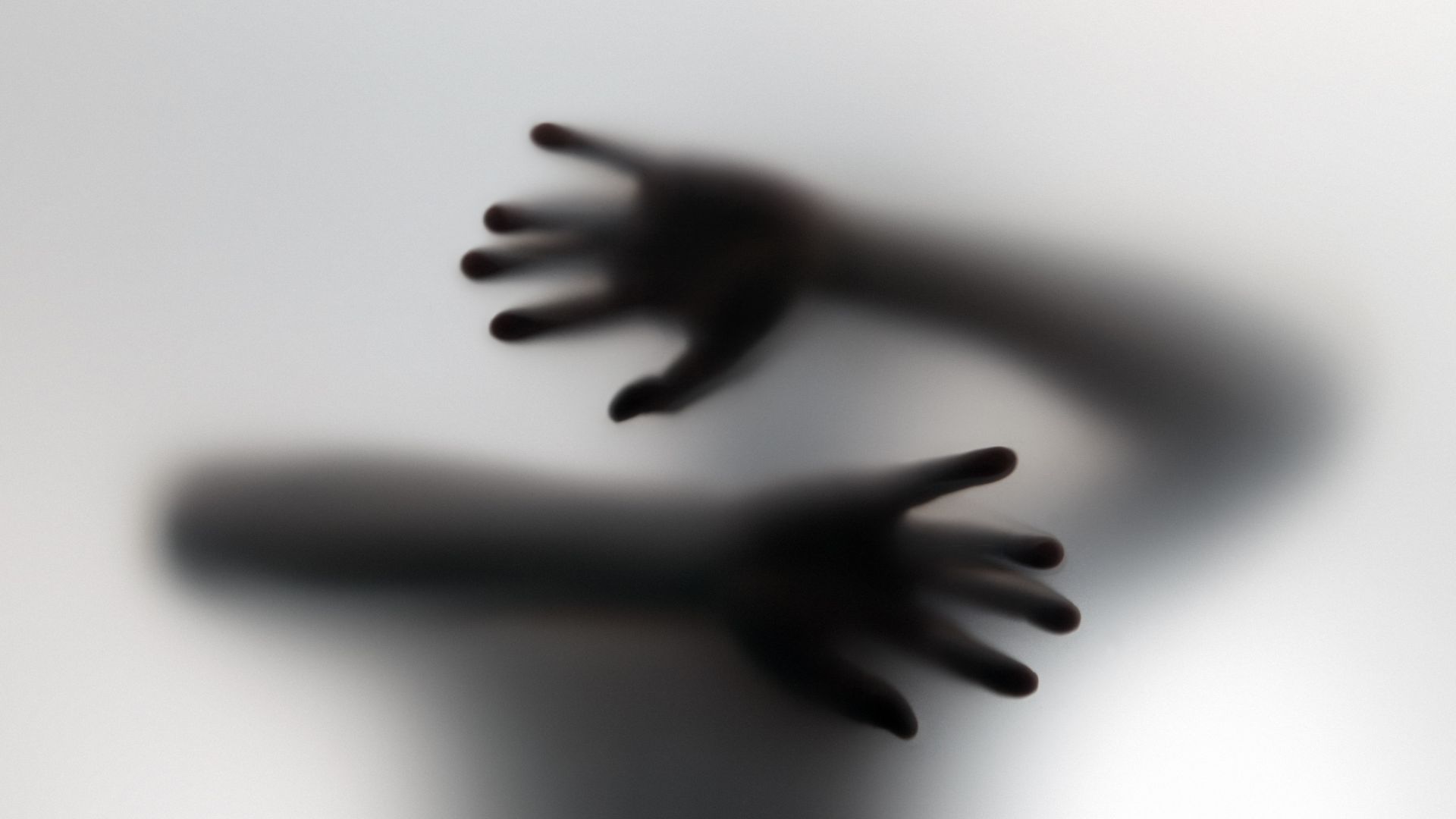 Soft focus black and white image showing blurred shadows of two hands with fingers spread reaching toward each other on light surface.