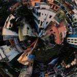 Spherical tiny planet 360 panorama showing dense urban residential area with colorful buildings, rooftops, narrow streets, and trees warping around central point in creative fisheye distortion effect.