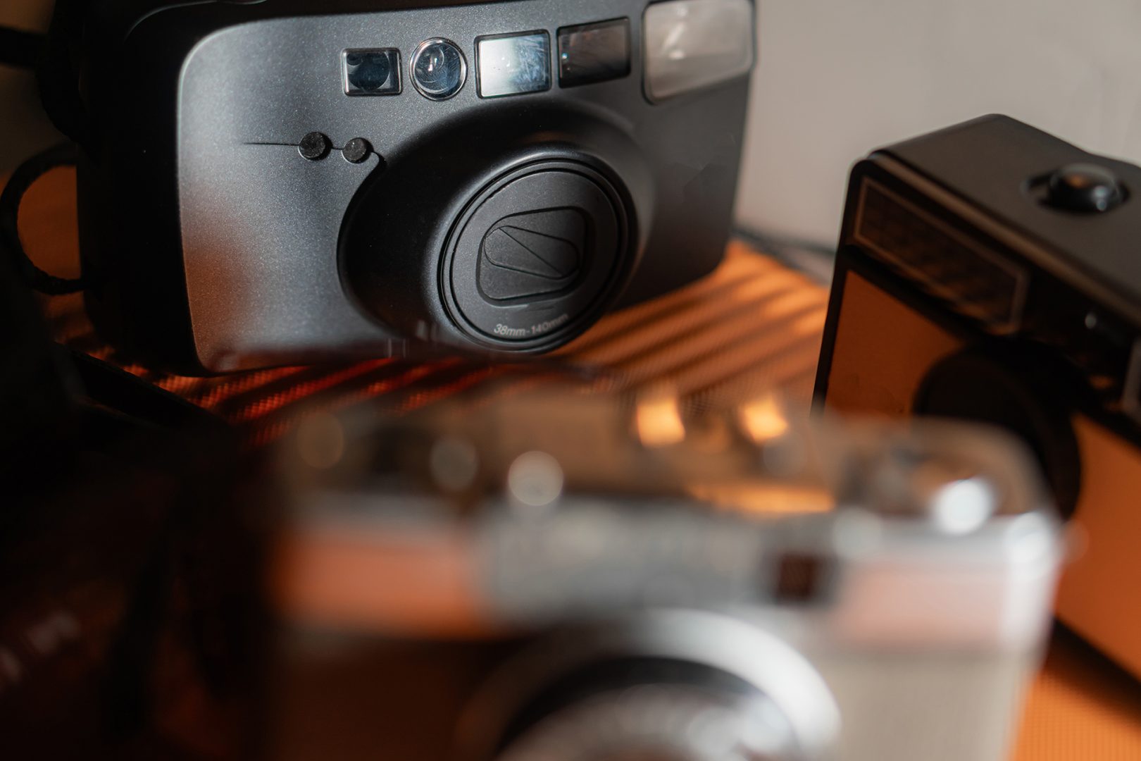 A close-up view of vintage cameras arranged on a surface, showcasing their unique designs and textures. The focus is on a prominent camera in the foreground, with others slightly blurred in the background.