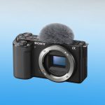 Front view of Sony ZV-E10 camera showing Alpha logo, E-mount visible sensor, textured grip, external shotgun microphone, recording buttons, and compact vlogging body.
