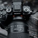 Black Sony mirrorless camera with FE 1.4/85 GM manual focus lens, mode dial, and control buttons visible on weathered wooden surface.