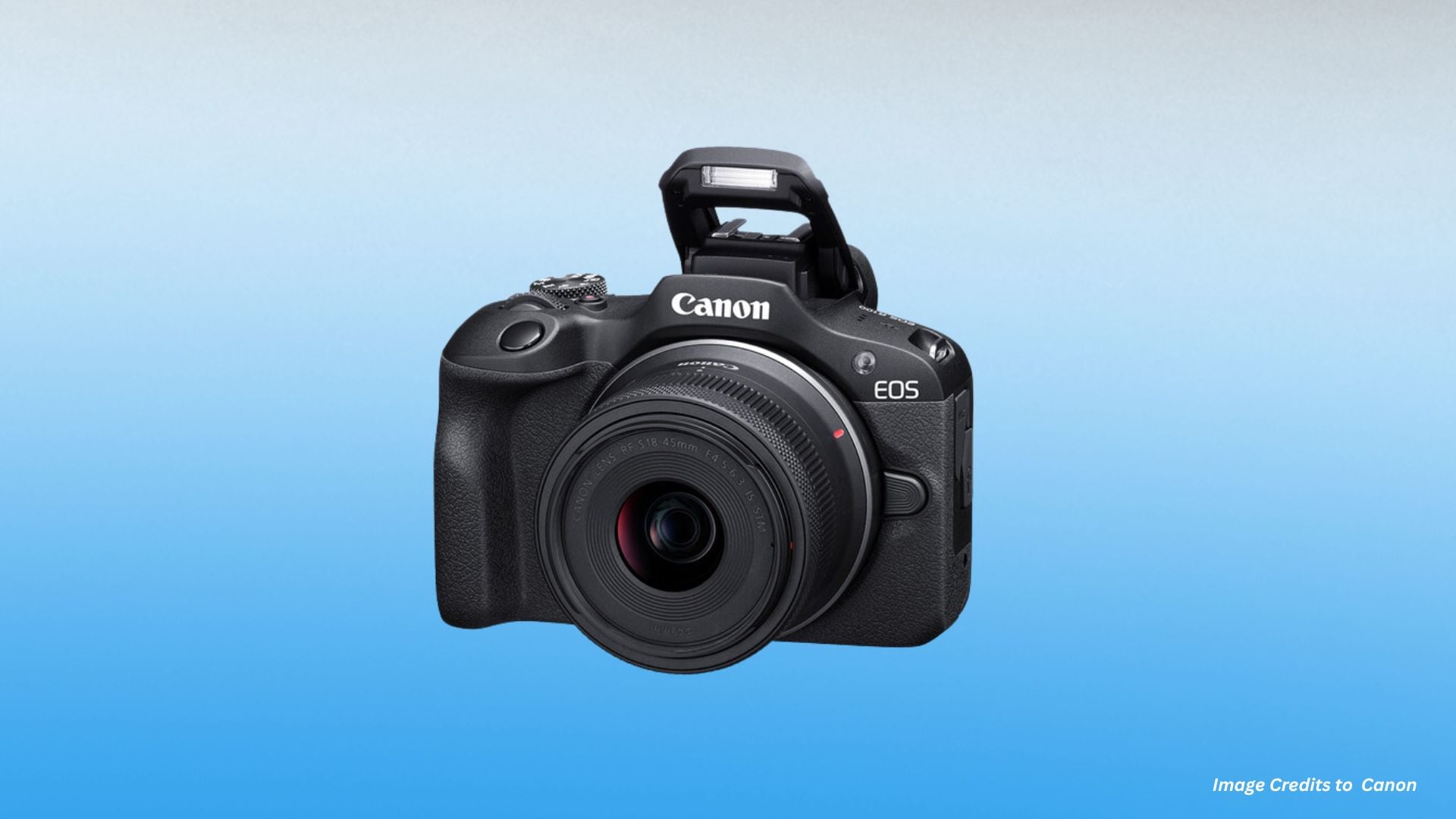 Three-quarter front view of Canon EOS R100 with RF-S 18-45mm lens and pop-up flash extended showing compact DSLR-style body design on blue background.