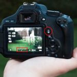 Hand holding camera showing LCD with outdoor scene. Red circles highlight exposure compensation button and scale displaying -2 to +1.33 stops adjustment range currently selected.