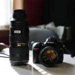 Nikon D750 camera body with attached prime lens beside tall telephoto zoom lens on desk. Professional photography equipment setup for various shooting scenarios.